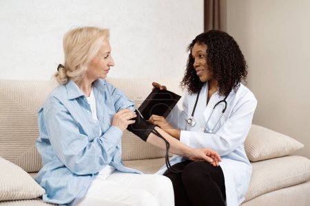 Freundliche Ärztin misst den Blutdruck älterer Patienten in gemütlicher Umgebung zu Hause