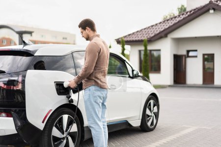 Man Charging Electric Car At Home Driveway
