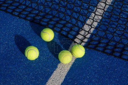 Téléchargez les photos : Foyer sélectif quatre balles de paddle tennis sur un court de paddle tennis bleu avec un filet en arrière-plan - en image libre de droit