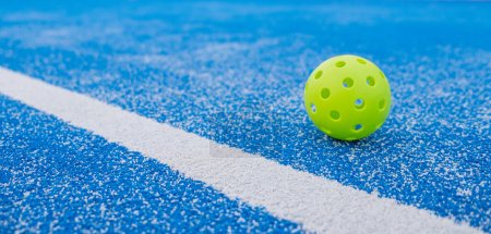 pickleball ball close to the line of a blue pickleball court, banner