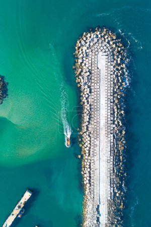 boat sailing near the breakwater of a harbor, top view from a drone