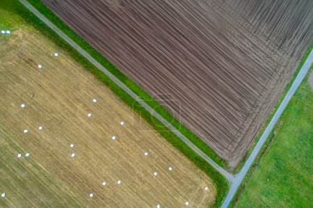 aerial top view of agricultural fields, one field plowed for planting and another harvested with round straw bales