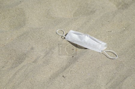 máscara quirúrgica que yace en la arena de una playa, concepto de ecología