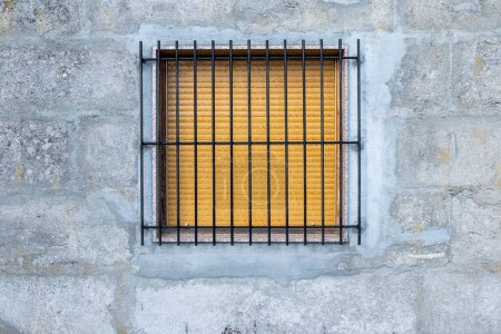 Fenêtre avec volet fermé et barres de fer sur un mur en béton.