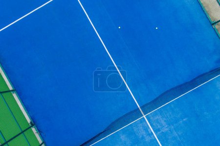 aerial drone photo of a blue paddle tennis court with balls on its surface