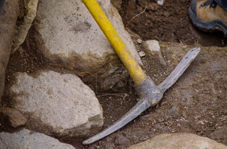 A yellow plastic-handled pick leaning against a wall during work at an archaeological excavation.