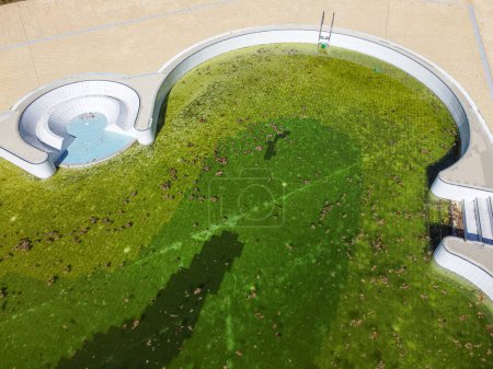 Luftaufnahme eines ungenutzten Schwimmbades mit grünem Wasser, Herbstzeit