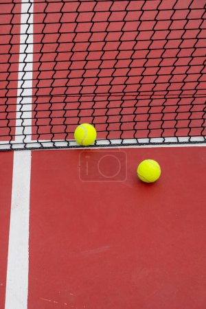 two balls near the net of a red tennis court