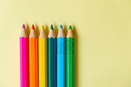 several colored pencils lined up on a pastel yellow background.