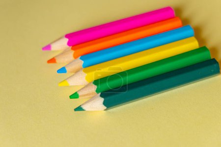 plusieurs crayons de couleur alignés sur un fond jaune pastel