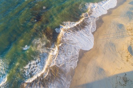 Drohne aus der Luft: Wellen brechen bei Sonnenaufgang am Ufer eines Strandes