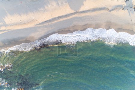 drone aerial overhead view of waves breaking on the shore of a beach at sunrise, summer background