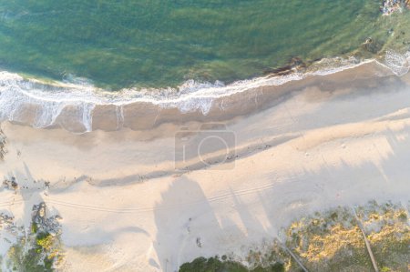 drone aerial top view of waves breaking on the shore of a beach at sunrise, summer background