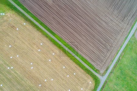 aerial top view of agricultural fields, one field plowed for planting and another harvested with round straw bales