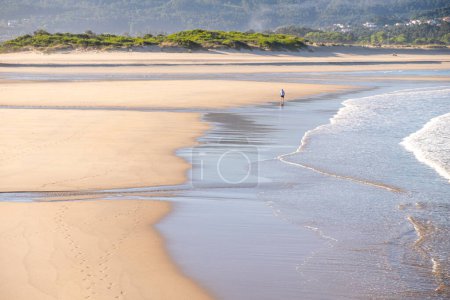 ein erwachsener Mann, der im Morgengrauen am Ufer eines Strandes spaziert