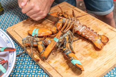 man's hand cutting lobster tails with a knife on a wooden board