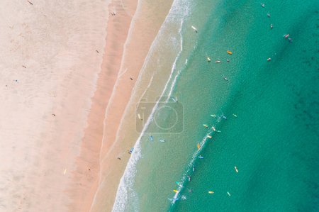 étudiants d'une école de surf sur le rivage d'une plage tôt le matin avec peu de personnes, vue aérienne avec un drone.
