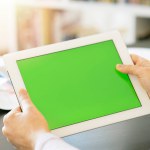 Mockup image of hands holding white tablet pc with white blank green screen on black table background in office