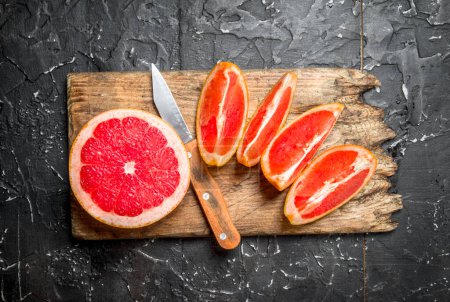 Photo for Pieces of grapefruit on a cutting Board with a knife. On rustic background - Royalty Free Image