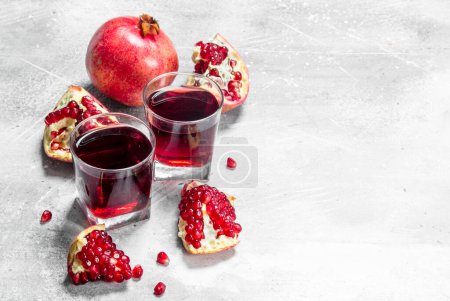 Pomegranate juice in a glass and pieces of pomegranate. On white rustic background