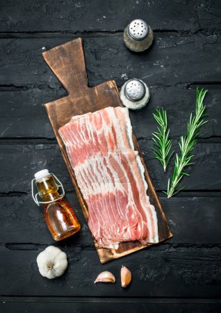 Photo for Raw bacon with rosemary branches. On black rustic background. - Royalty Free Image