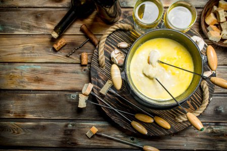 Delicious fondue cheese with olives and white wine.On a wooden background.
