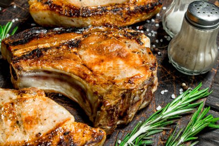 Téléchargez les photos : Biftecks de porc grillés au romarin et au sel sur une vieille planche. Sur un fond en bois
. - en image libre de droit