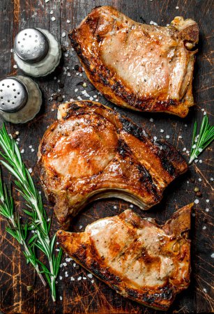 Biftecks de porc grillés au romarin et au sel sur une vieille planche. Sur un fond en bois
.