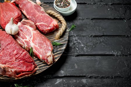 Téléchargez les photos : Viande crue. Biftecks de porc et de bœuf sur un plateau avec des épices et du romarin. Sur un fond rustique noir
. - en image libre de droit