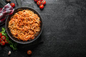Spaghetti with Bolognese sauce in pan with napkin, tomatoes and garlic. On black rustic background Poster #657780544