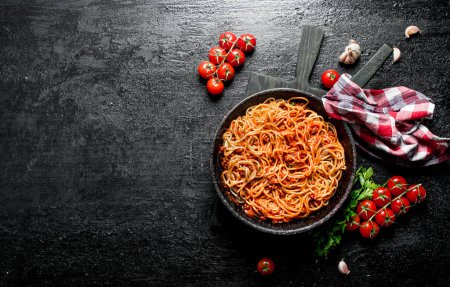 Spaghetti with Bolognese sauce in pan with napkin, tomatoes and garlic. On black rustic background Poster 657780636