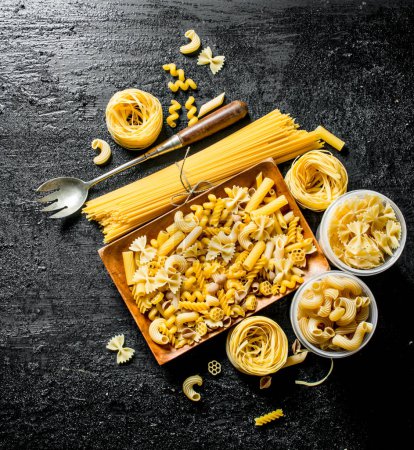 Photo for Different types of dry pasta on the plate and bowls. On black rustic background - Royalty Free Image