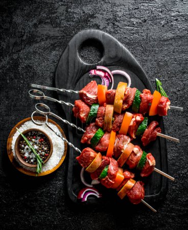Téléchargez les photos : Kebab cru aux légumes, épices et tranches d'oignon. Sur fond rustique noir - en image libre de droit