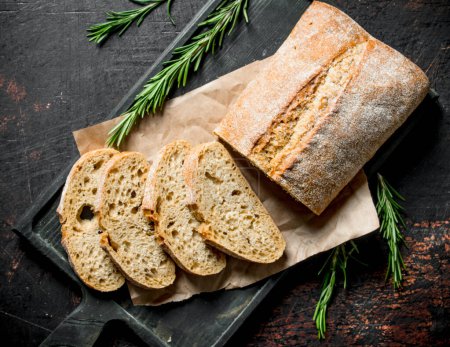 Photo for Sliced ciabatta bread on a cutting Board with rosemary. On dark rustic background - Royalty Free Image
