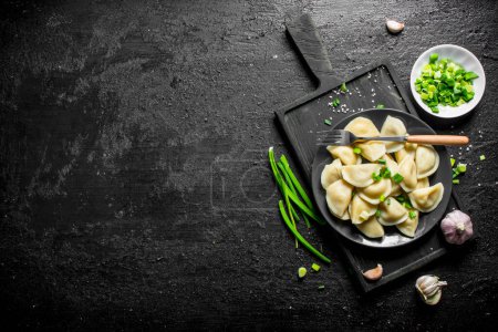 Foto de Dumplings en un plato con cebollas verdes y ajo. Sobre fondo rústico negro - Imagen libre de derechos