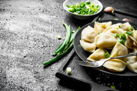 Foto de Dumplings con cebollas verdes picadas y rodajas de ajo. Sobre fondo rústico negro - Imagen libre de derechos