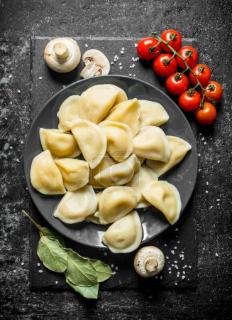 Dumplings on a plate and cherry tomatoes. On dark rustic background