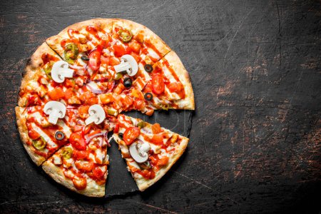 Plastry chrupiącą pizzę z pomidorów, papryki i grzybów. Na ciemnym tle rustykalnym