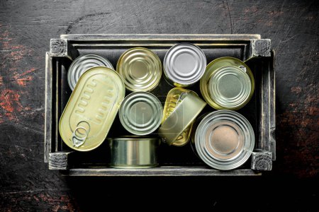 Photo for Canned food in closed cans in a box. On dark rustic background - Royalty Free Image