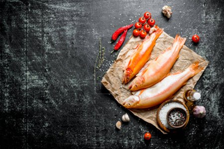 Raw trout fish on paper with tomatoes, chili pepper and spices. On dark rustic background