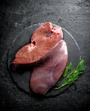 Raw liver with dill on a stone Board. On black rustic background