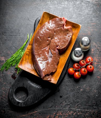 Raw liver with herbs, tomatoes and spices on the cutting Board. On dark rustic background