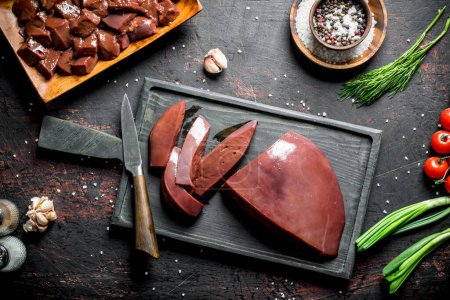 Sliced raw liver on a cutting Board with a knife. On dark rustic background
