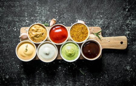 Photo for Sauces on a wooden cutting Board with garlic and rosemary. On dark rustic background - Royalty Free Image