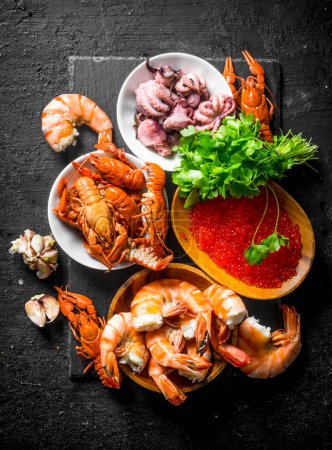 Seafood. Shrimp, crayfish, octopus and caviar with parsley and garlic cloves. On black rustic background