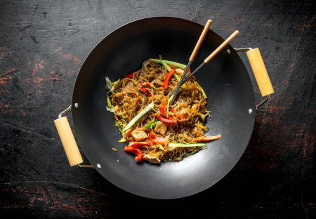 Fragrant Chinese cellophane noodles in a frying pan wok with salmon and vegetables. On dark rustic background