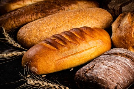 Téléchargez les photos : Différents types de pain avec des épillets. Sur un fond sombre. Photo de haute qualité - en image libre de droit
