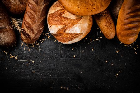 Téléchargez les photos : Différents types de pain frais sur la table. Sur fond noir. Photo de haute qualité - en image libre de droit