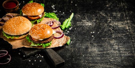 Téléchargez les photos : Burger on a cutting board with onion rings, tomato sauce and lettuce. On a black background. - en image libre de droit