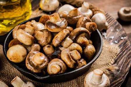 Téléchargez les photos : Frying pan with fried mushrooms on a wooden tray. On a wooden background. High quality photo - en image libre de droit